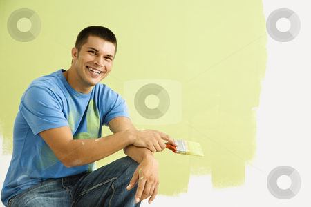 Smiling painting man. Smiling painting man. stock photo, Smiling man kneeling in front of partially painted wall holding paintbrush. by Iofoto Images