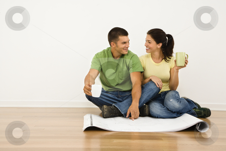 Couple renovating. Couple renovating. stock photo, Attractive couple sitting on home floor with coffee cups looking at house plans and smiling at eachother. by Iofoto Images