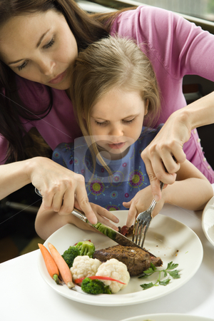 Mom helping daughter cut food. Mom helping daughter cut food. stock photo, Caucasian mother helping cut meat for her daughter. by Iofoto Images