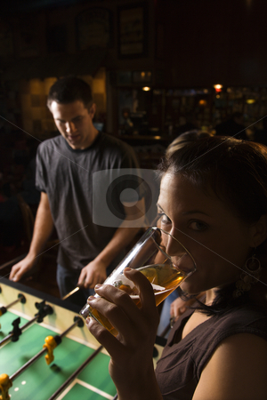 To use this stock image in your creative project, please select the size you need over to the right and click the "Add to Cart" button.
Your downloaded image will come with the Cutcaster watermark removed so don’t worry about the watermark you see on this page. Woman drinking beer. stock photo, Young woman drinking beer and looking at viewer while man plays foosball in pub. by Iofoto Images