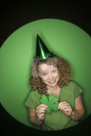Woman holding shamrock. Woman holding shamrock. stock photo, Vignette of smiling young adult Caucasian woman on green background wearing Saint Patricks Day hat and holding shamrock. by Iofoto Images