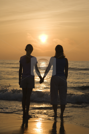 Mom and daughter at sunrise. Mom and daughter at sunrise. stock photo, Caucasian mid- female and teenage daughter standing on beach at sunset holding hands. by Iofoto Images