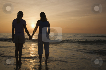 Mom and daughter at sunrise. Mom and daughter at sunrise. stock photo, Caucasian mid-adult mother teenage and daughter standing on beach at sunset holding hands. by Iofoto Images