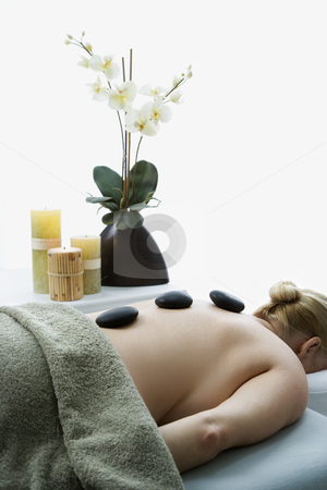 Hot stone massage. Hot stone massage. stock photo, Caucasian middle-aged woman lying on massage table with hot stones on her back. by Iofoto Images