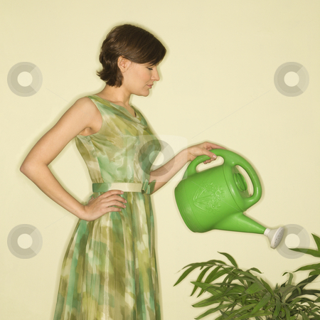 Woman watering plant. Woman watering plant. stock photo, Pretty Caucasian mid-adult woman wearing vintage dress watering houseplant with green watering can. by Iofoto Images