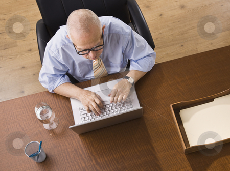 Elderly man on Laptop Elderly man on Laptop stock photo, An elderly man is seated at a desk and is working on a laptop. He is looking away from the camera. Horizontally framed shot. by Jonathan Ross