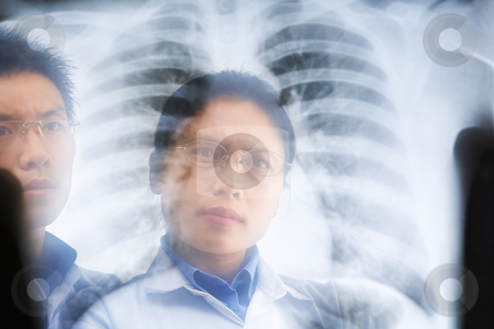 Two Asian doctor examining xray result Two Asian doctor examining xray result stock photo, Two Asian doctor examining xray result. PS:the image taken from behind the xray print, so it may leave some soft noise on the people image behind it. by Rudyanto Wijaya