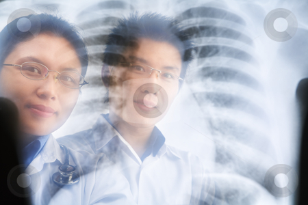 Two Asian doctor smiling through the xray result Two Asian doctor smiling through the xray result stock photo, Two Asian doctor smiling through the xray result. PS:the image taken from behind the xray print, so it may leave some soft noise on the people image behind it. by Rudyanto Wijaya