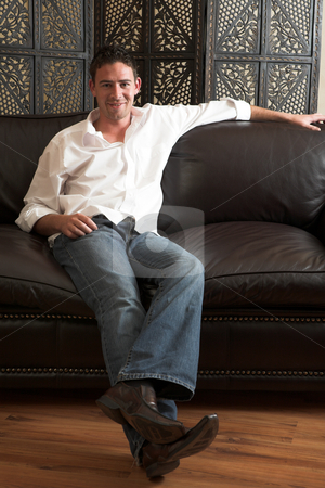 Relaxed young man Relaxed young man stock photo, Relaxed young adult male wearing blue jeans, a loose white cotton shirt and sitting comfortable on a leather couch by Sean Nel