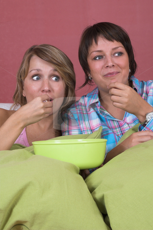 Shocking event Shocking event stock photo, Two girls on the couch together watching a movie while eating popcorn and looking surprised by Simone Van den Berg