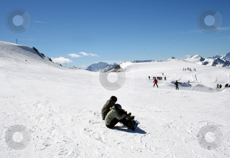 Skiers on Alpine ski slope Skiers on Alpine ski slope stock photo, Two skiers resting on Alpine ski slope with people skiing in background. by Martin Crowdy