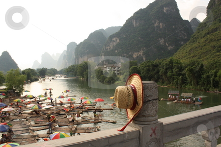 Bamboo rafting on Li-river, Yangshou, China Bamboo rafting on Li-river, Yangshou, China stock photo, Bamboo raft with tourists on the Li-river, the view from the bridge with a straw hat, Yangshou, China by Yulia Zhukova