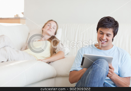 To use this stock image in your creative project, please select the size you need over to the right and click the "Add to Cart" button.
Your downloaded image will come with the Cutcaster watermark removed so don’t worry about the watermark you see on this page. Young man using a tablet computer while his girlfriend is sleepi stock photo, Young man using a tablet computer while his girlfriend is sleeping in their living room by Wavebreak Media