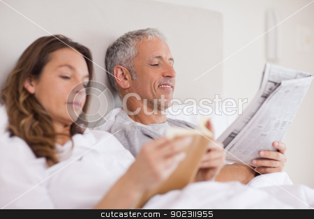 To use this stock image in your creative project, please select the size you need over to the right and click the "Add to Cart" button.
Your downloaded image will come with the Cutcaster watermark removed so don’t worry about the watermark you see on this page. Happy woman reading a book while her husband is reading a newspa stock photo, Happy woman reading a book while her husband is reading a newspaper in their bedroom by Wavebreak Media