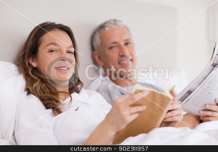To use this stock image in your creative project, please select the size you need over to the right and click the "Add to Cart" button.
Your downloaded image will come with the Cutcaster watermark removed so don’t worry about the watermark you see on this page. Smiling woman reading a book while her husband is reading the ne stock photo, Smiling woman reading a book while her husband is reading the news in their bedroom by Wavebreak Media