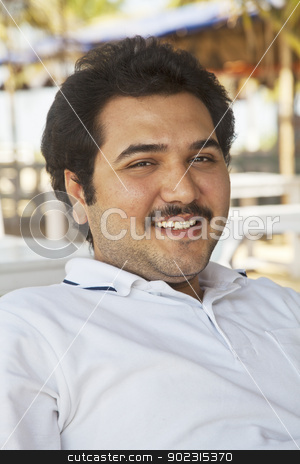 To use this stock image in your creative project, please select the size you need over to the right and click the "Add to Cart" button.
Your downloaded image will come with the Cutcaster watermark removed so don’t worry about the watermark you see on this page. Smiling young adult male relaxed posture stock photo, vertical portrait of a smiling young adult male, combed back hair, mustache, unshaved, celebrity look a like, showing teeth, wearing white pole shirt, in the shade outdoors leaning back in a relaxed posture by Kantilal Patel