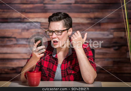 To use this stock image in your creative project, please select the size you need over to the right and click the "Add to Cart" button.
Your downloaded image will come with the Cutcaster watermark removed so don’t worry about the watermark you see on this page. Shocked Butch Woman with Phone stock photo, Serious woman wearing flannel shirt looking at smart phone and seated in front of modern desk at hipster office by Scott Griessel