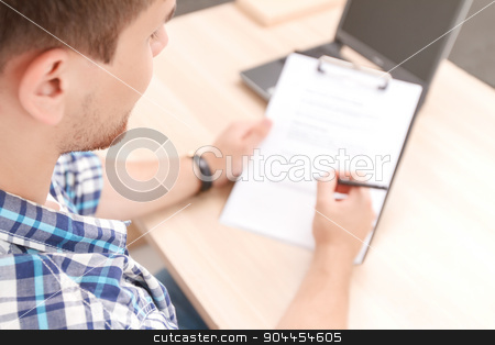 To use this stock image in your creative project, please select the size you need over to the right and click the "Add to Cart" button.
Your downloaded image will come with the Cutcaster watermark removed so don’t worry about the watermark you see on this page. Young student working on project stock photo, Top view of a young student sitting at the table holding a folder and filling some information for his project work by Zinkevych