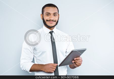 To use this stock image in your creative project, please select the size you need over to the right and click the "Add to Cart" button.
Your downloaded image will come with the Cutcaster watermark removed so don’t worry about the watermark you see on this page. Freestyle photo with young mulatto stock photo, Young mixed race businessman with beard standing on grey background. Young man smiling and holding tablet computer by Dmytro Sidelnikov