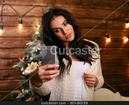 To use this stock image in your creative project, please select the size you need over to the right and click the "Add to Cart" button.
Your downloaded image will come with the Cutcaster watermark removed so don’t worry about the watermark you see on this page. people, holidays and technology concept - beautiful brunette woman in white sweater taking selfie picture by smartphone over christmas tree and living room background stock photo, people, holidays and technology concept - beautiful brunette woman in white Christmas sweater taking selfie picture by smartphone over christmas tree living room background by mykhalets