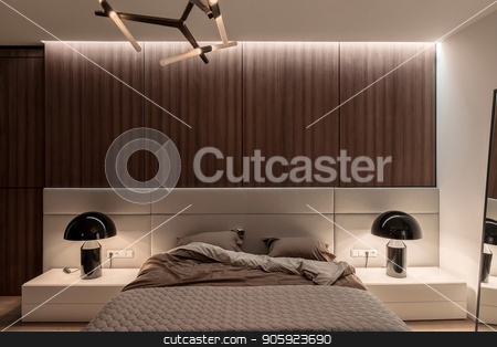 To use this stock image in your creative project, please select the size you need over to the right and click the "Add to Cart" button.
Your downloaded image will come with the Cutcaster watermark removed so don’t worry about the watermark you see on this page. Stylish modern bedroom stock photo, Bedroom in a modern style with white and wooden walls, parquet on a floor and luminous fancy lamps. There is a bed with a brown linens and a gray plaid, mirror, night stands. Horizontal. by bezikus