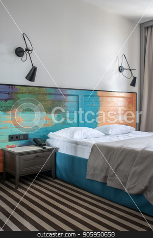 To use this stock image in your creative project, please select the size you need over to the right and click the "Add to Cart" button.
Your downloaded image will come with the Cutcaster watermark removed so don’t worry about the watermark you see on this page. Beautiful hotel room stock photo, Stylish room in a hotel with light walls and striped floor. There is a blue double bed with a colorful wooden bedhead, dark gray nightstand with a phone, black lamps on the wall. Vertical. by bezikus