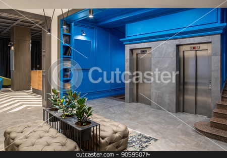 To use this stock image in your creative project, please select the size you need over to the right and click the "Add to Cart" button.
Your downloaded image will come with the Cutcaster watermark removed so don’t worry about the watermark you see on this page. Stylish interior in hotel stock photo, Amazing hallway in the hotel with blue walls and a tiled floor. There are two lifts, brown stair, shelves with books, black stand with green plants in the pots, sofas, luminous lamps, reception desk. by bezikus