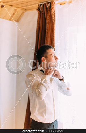 To use this stock image in your creative project, please select the size you need over to the right and click the "Add to Cart" button.
Your downloaded image will come with the Cutcaster watermark removed so don’t worry about the watermark you see on this page. Half-length portrait of the groom tying the bow-tie while looking through the window. stock photo, Half-length portrait of the groom tying the bow-tie while looking through the window by Andrii Kobryn