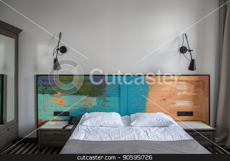 To use this stock image in your creative project, please select the size you need over to the right and click the "Add to Cart" button.
Your downloaded image will come with the Cutcaster watermark removed so don’t worry about the watermark you see on this page. Stylish hotel room stock photo, Beautiful room in a hotel with light walls and striped floor. There is a blue double bed with a colorful wooden bedhead, dark gray nightstands, black lamps on the wall, wardrobe with a mirror. by bezikus