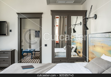 To use this stock image in your creative project, please select the size you need over to the right and click the "Add to Cart" button.
Your downloaded image will come with the Cutcaster watermark removed so don’t worry about the watermark you see on this page. Beautiful hotel room stock photo, Stylish hotel room with light walls and a striped floor. There is a double bed with a colorful wooden bedhead, dark gray wardrobe with mirrors, stand, black lamps on the wall, blue table, TVs. by bezikus
