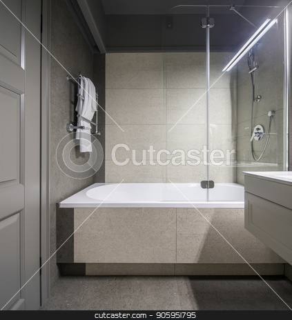 To use this stock image in your creative project, please select the size you need over to the right and click the "Add to Cart" button.
Your downloaded image will come with the Cutcaster watermark removed so don’t worry about the watermark you see on this page. Stylish bathroom in hotel stock photo, Stylish bathroom with light tiled walls. There is a white bath with a shower and a glass partition, chrome towel rack, sink, gray door, luminous lamps. Vertical. by bezikus