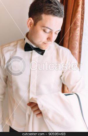 To use this stock image in your creative project, please select the size you need over to the right and click the "Add to Cart" button.
Your downloaded image will come with the Cutcaster watermark removed so don’t worry about the watermark you see on this page. The groom is looking aside while standing near the window. stock photo, The groom is looking aside while standing near the window by Andrii Kobryn