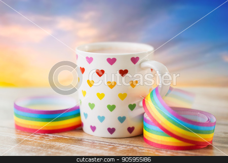 To use this stock image in your creative project, please select the size you need over to the right and click the "Add to Cart" button.
Your downloaded image will come with the Cutcaster watermark removed so don’t worry about the watermark you see on this page. cup with heart pattern and gay awareness ribbon stock photo, homosexual and lgbt concept - close up of cup with rainbow colored heart pattern and gay pride awareness ribbon on wooden table over evening sky background by Syda Productions