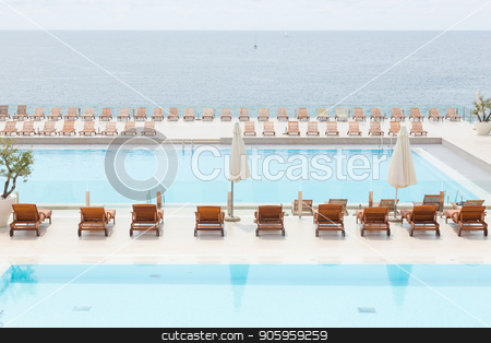 To use this stock image in your creative project, please select the size you need over to the right and click the "Add to Cart" button.
Your downloaded image will come with the Cutcaster watermark removed so don’t worry about the watermark you see on this page. Luxury swimming pool with wooden deck chairs. stock photo, Luxury swimming pool with wooden sunbeds and umbrellas. by kasto