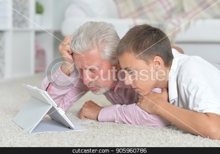 To use this stock image in your creative project, please select the size you need over to the right and click the "Add to Cart" button.
Your downloaded image will come with the Cutcaster watermark removed so don’t worry about the watermark you see on this page. Grandfather with grandson using tablet while lying on floor stock photo, Grandfather with grandson using tablet while lying on floor at home by Ruslan Huzau
