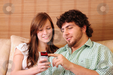 To use this stock image in your creative project, please select the size you need over to the right and click the "Add to Cart" button.
Your downloaded image will come with the Cutcaster watermark removed so don’t worry about the watermark you see on this page. Young couple pointing at mobile phone stock photo, Young couple sitting on a couch, pointing at a mobile phone. by Nicolaas Traut