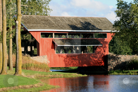 To use this stock image in your creative project, please select the size you need over to the right and click the "Add to Cart" button.
Your downloaded image will come with the Cutcaster watermark removed so don’t worry about the watermark you see on this page. 1800's Red Covered Bridge stock photo, Red wooden 1800's era covered bridge set in a park like setting. Surrounded by green grass, mature trees, stonework and a beautiful lake. by Betty Hansen