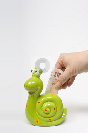 To use this stock image in your creative project, please select the size you need over to the right and click the "Add to Cart" button.
Your downloaded image will come with the Cutcaster watermark removed so don’t worry about the watermark you see on this page. Saving Money stock photo, A female hand deposits a UK ??10 banknote into a green, snail shaped money box symbolising slow sure progress in investment. by Steve Smith