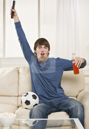 To use this stock image in your creative project, please select the size you need over to the right and click the "Add to Cart" button.
Your downloaded image will come with the Cutcaster watermark removed so don’t worry about the watermark you see on this page. Man Cheering at Game stock photo, A young man is sitting on the couch in his living room and watching a sports game. He is holding a remote control, a soda, and there is a soccer ball right next to him. He is looking at the camera. Vertically framed shot. by Jonathan Ross