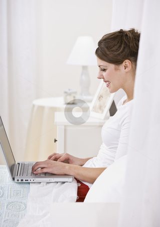 To use this stock image in your creative project, please select the size you need over to the right and click the "Add to Cart" button.
Your downloaded image will come with the Cutcaster watermark removed so don’t worry about the watermark you see on this page. Attractive Brunette Using Laptop stock photo, The side view of an attractive young brunette using a laptop in bed. She is smiling at the screen. Vertically framed shot. by Jonathan Ross