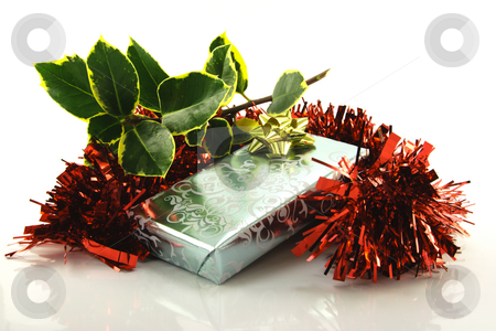 To use this stock image in your creative project, please select the size you need over to the right and click the "Add to Cart" button.
Your downloaded image will come with the Cutcaster watermark removed so don’t worry about the watermark you see on this page. Gift with Holly and Tinsel stock photo, Single shiny silver wrapped gift with gold bow, green holly and red tinsel on a reflective white background by Keith Wilson