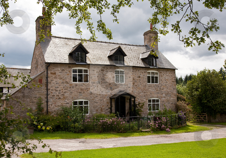 To use this stock image in your creative project, please select the size you need over to the right and click the "Add to Cart" button.
Your downloaded image will come with the Cutcaster watermark removed so don’t worry about the watermark you see on this page. Old stone cottage surrounded by trees and roses stock photo, Rough stone house with dormer windows and surrounding flowers and roses by Steven Heap