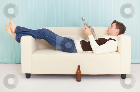 Person Reads Magazine Comfortably Lying On Sofa Stock Photo