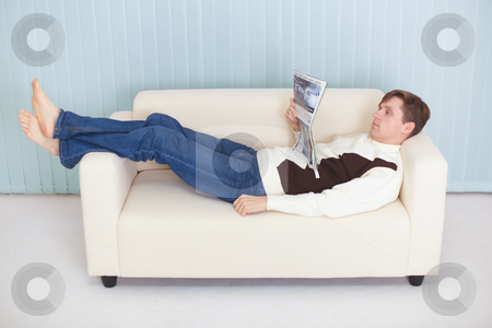 Young Man Reads Magazine Lying On Couch Stock Photo